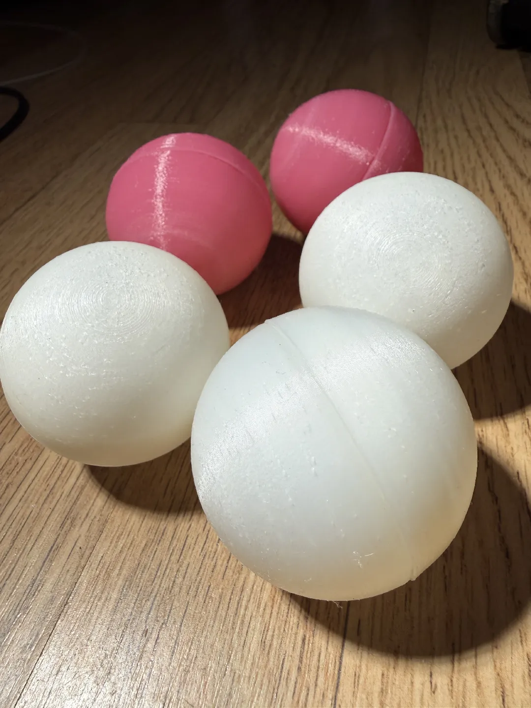 Four finished 3D-printed juggling balls, two white and two pink, on a wooden floor