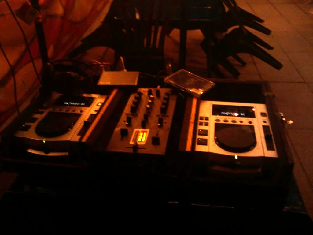 Two Pioneer CDJ-100S CD decks with a mixer between them, set into a flight case on a bar floor